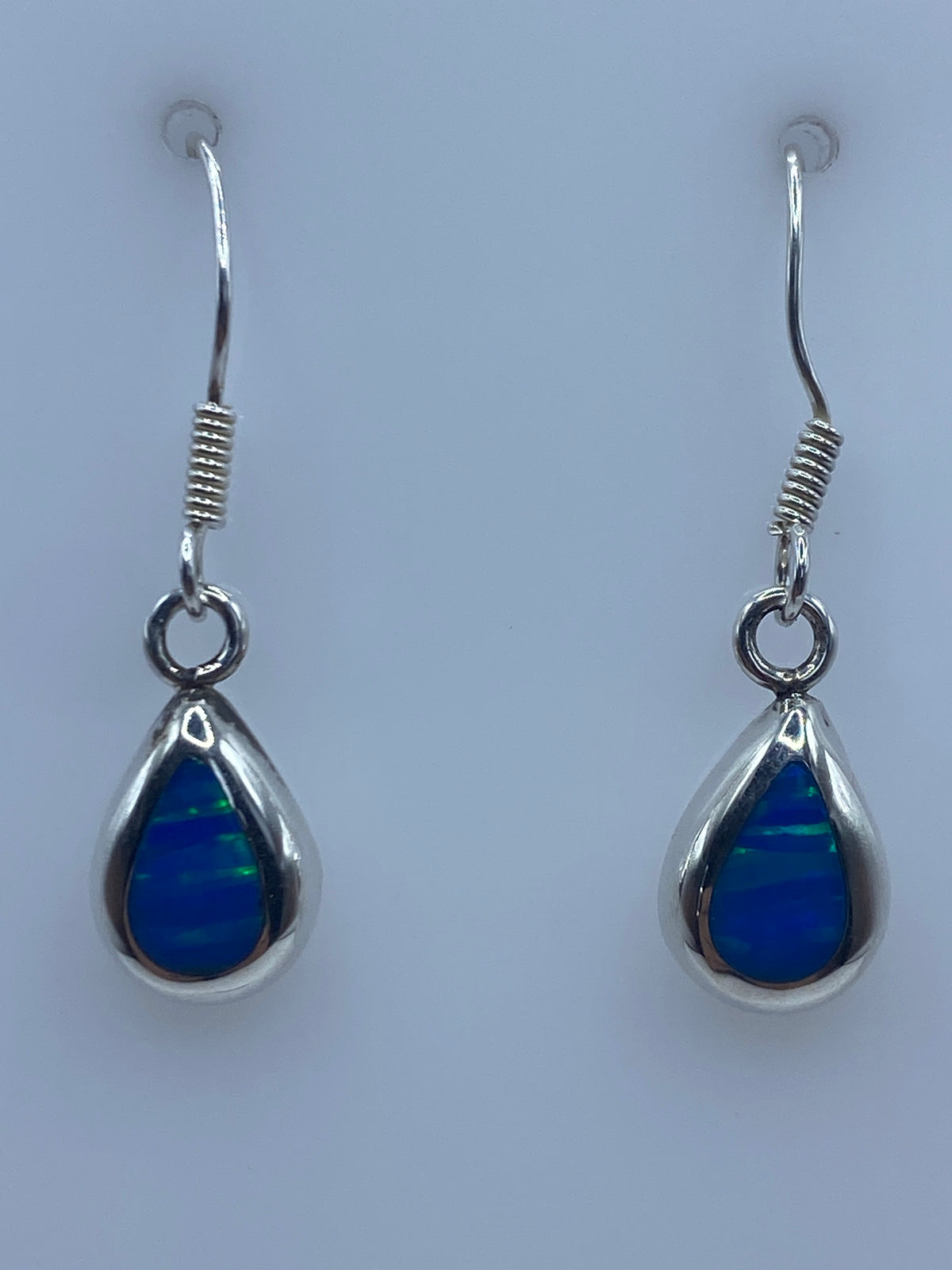 Par de aretes de plata 925 con ópalo de fuego azul brillante colgando en fondo neutro