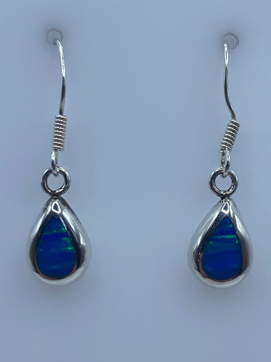 Par de aretes de plata 925 con ópalo de fuego azul brillante colgando en fondo neutro