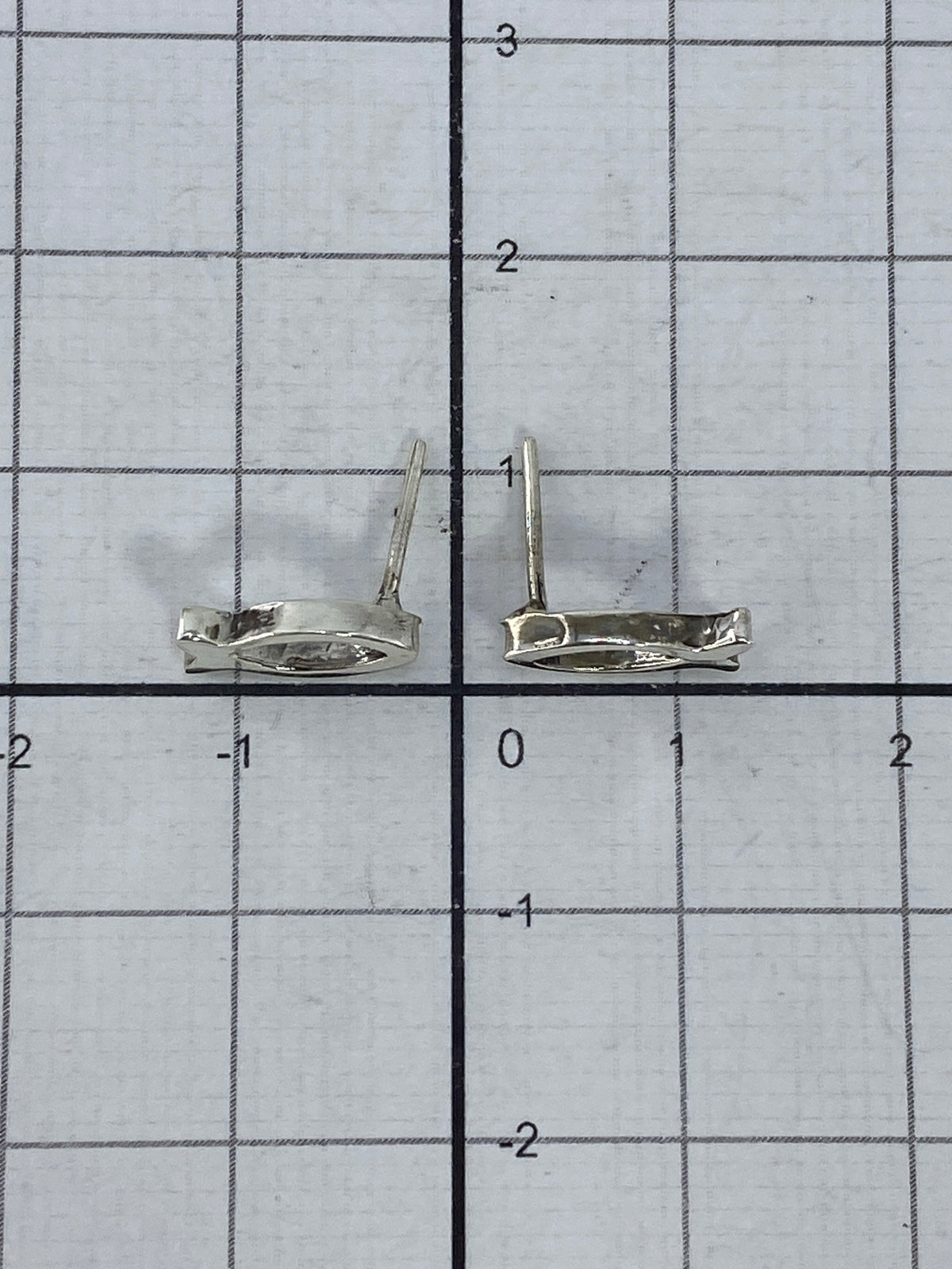 Aretes de plata pez colocados sobre una regla milimetrada, mostrando su escala