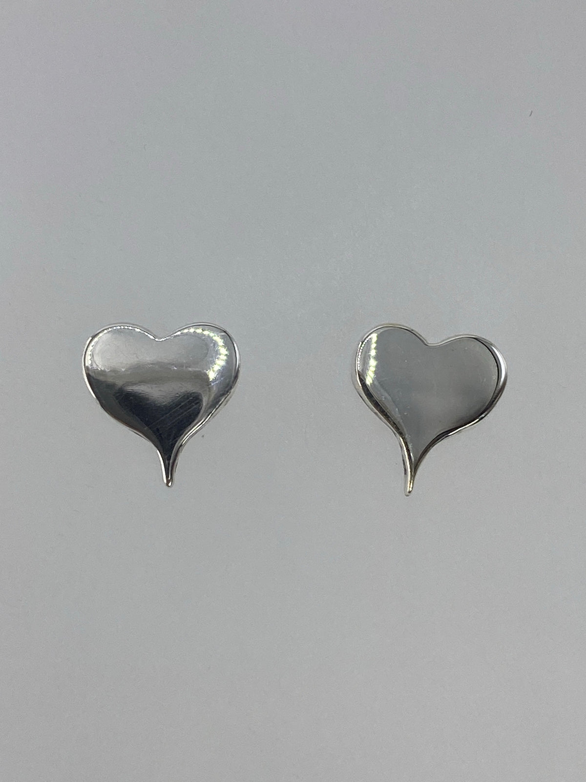 Aretes de plata corazón cartoneado en posición frontal, par completo