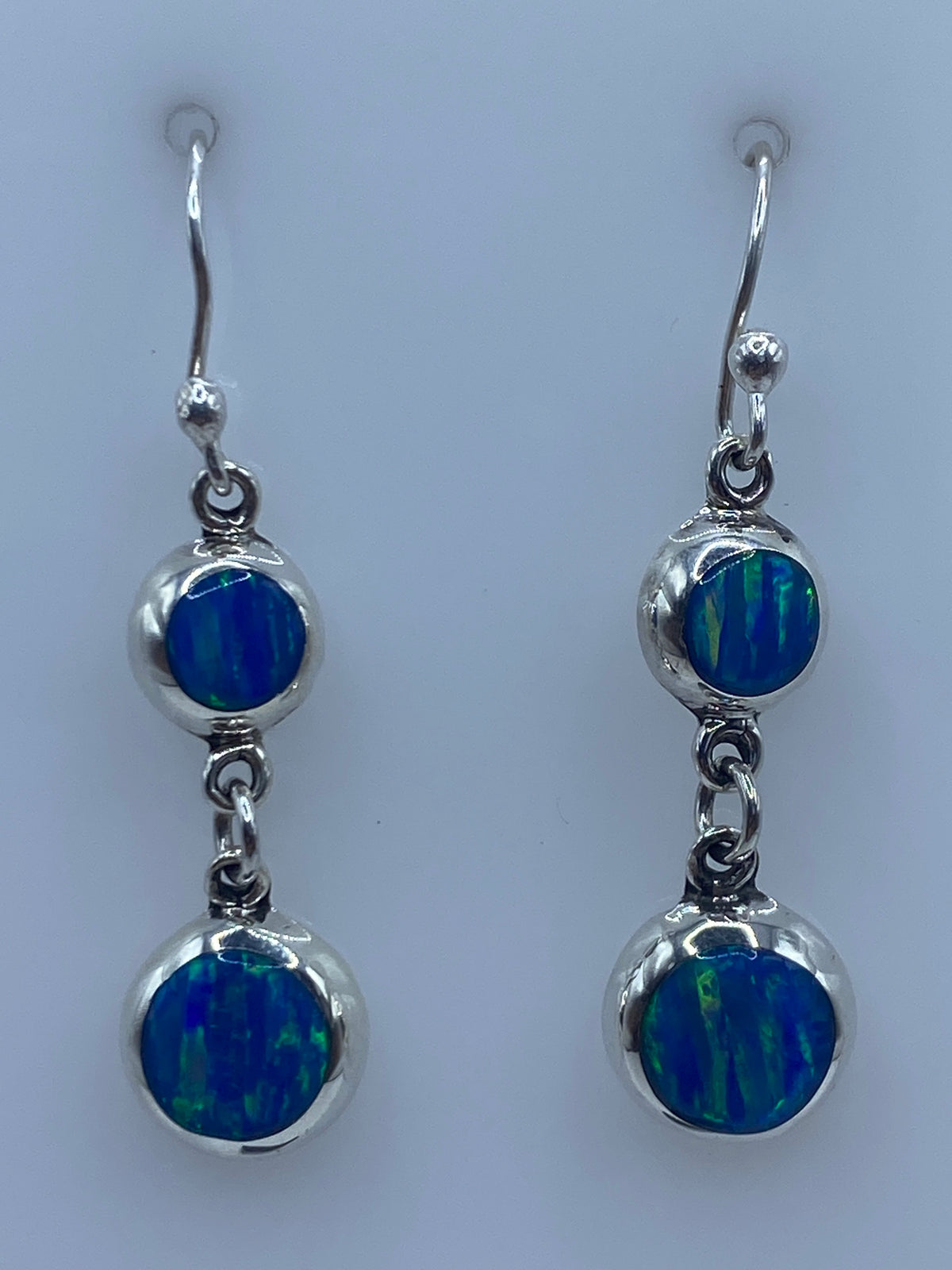 Par de aretes plata ópalo de fuego azul, incrustación a mano, colgando sobre superficie gris