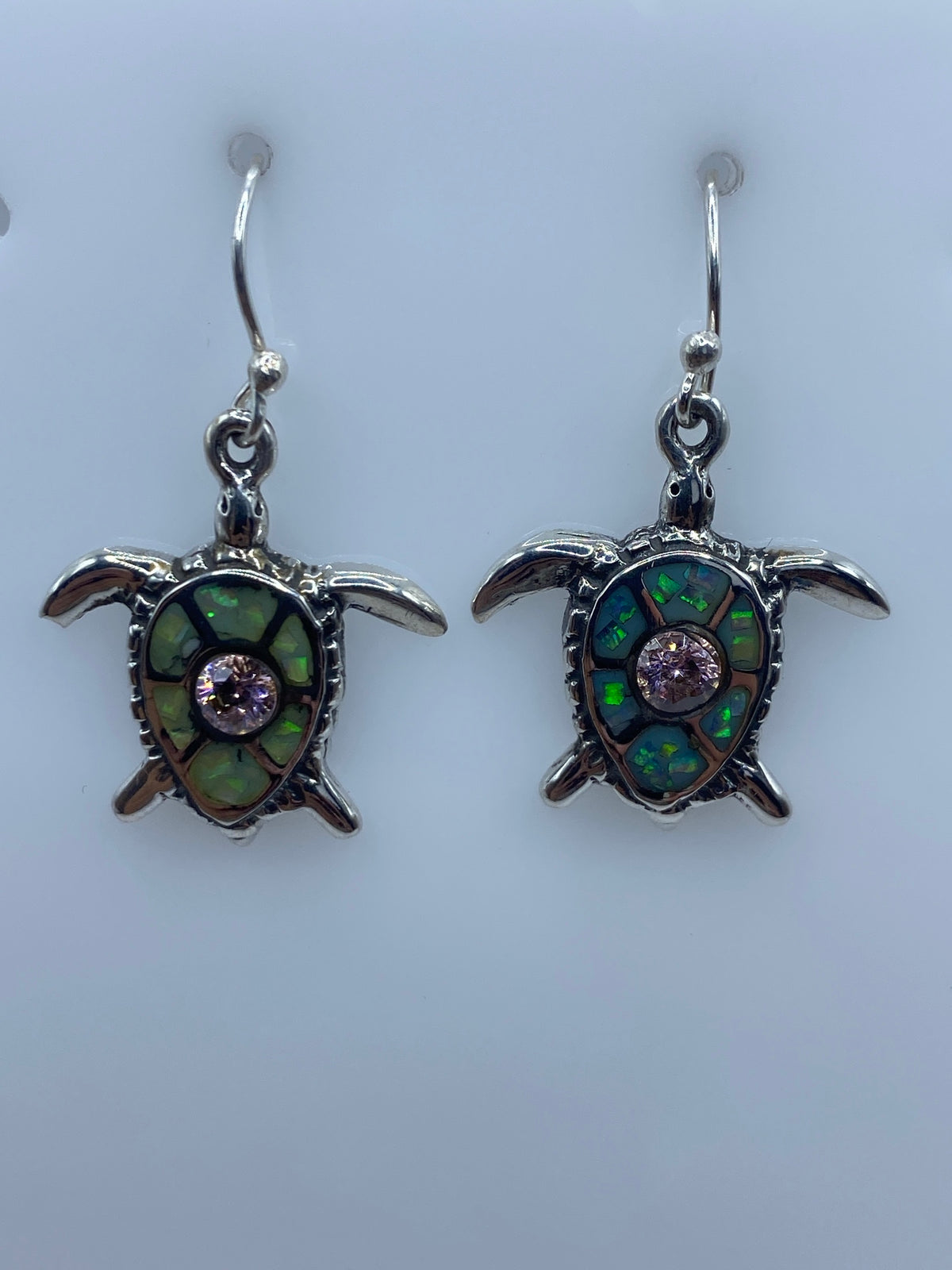 Arete tortuga con ópalo de fuego mostrando tonos verdes y morados bajo luz