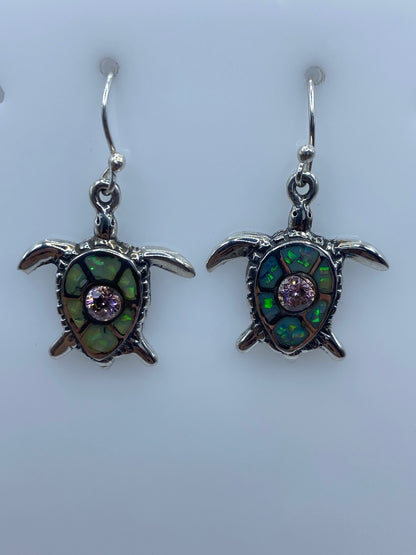 Arete tortuga con ópalo de fuego mostrando tonos verdes y morados bajo luz