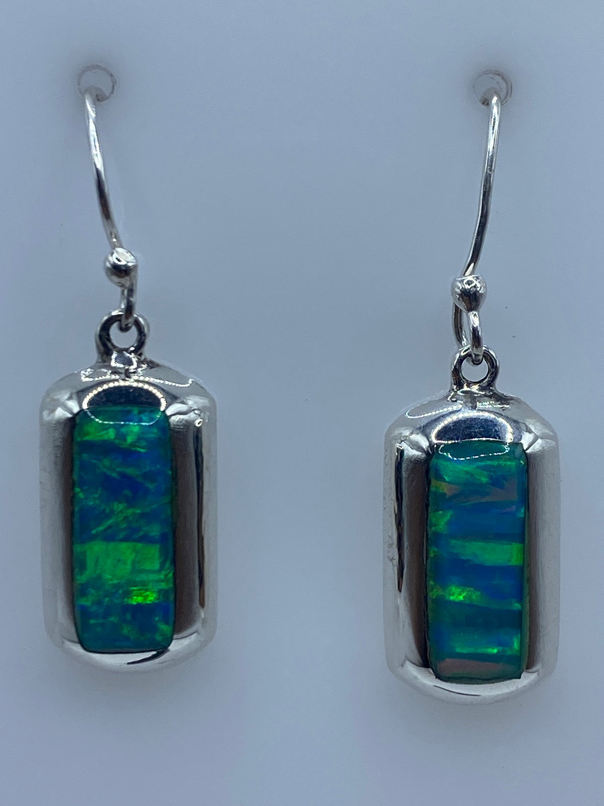 Par de aretes de plata 925 con ópalo de fuego azul cielo engastado, colgando sobre fondo blanco