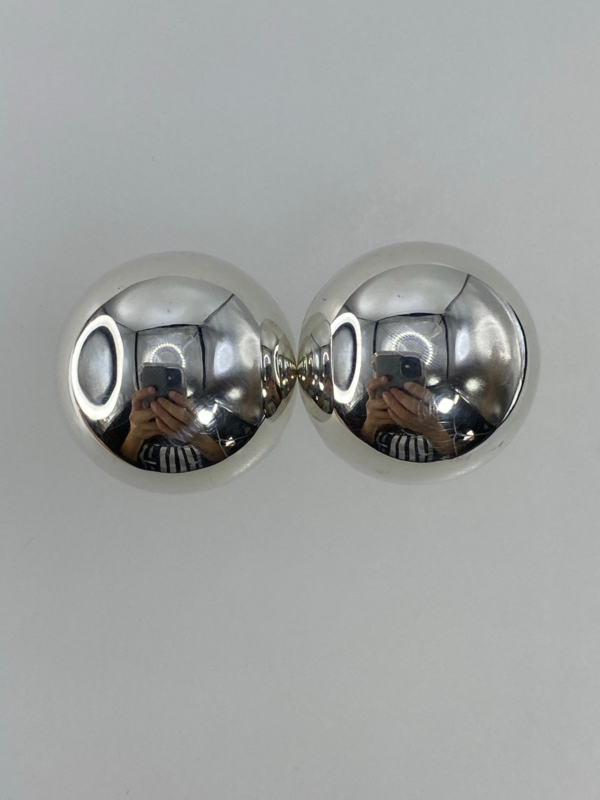 Par de aretes de plata cartoneado, esféricos y brillantes, sobre fondo blanco