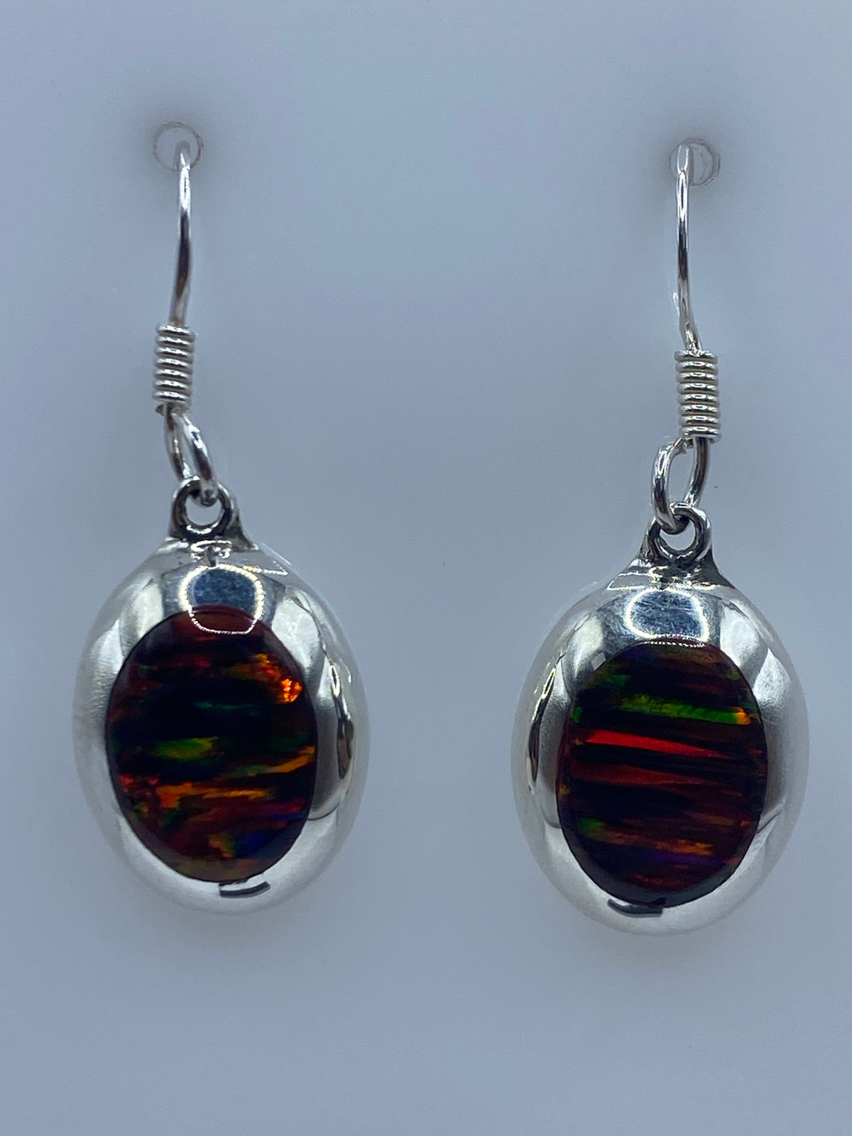 Aretes de plata con opalo de fuego en detalle mostrando los reflejos naranja, rojo y verde