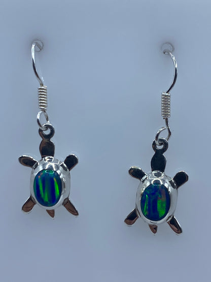 Par de aretes de plata con ópalo de fuego azul en forma de tortuga, colgando de los ganchos