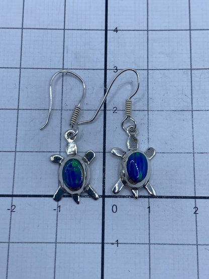 Aretes de tortuga con ópalo azul sobre fondo gris, medidas y peso visibles