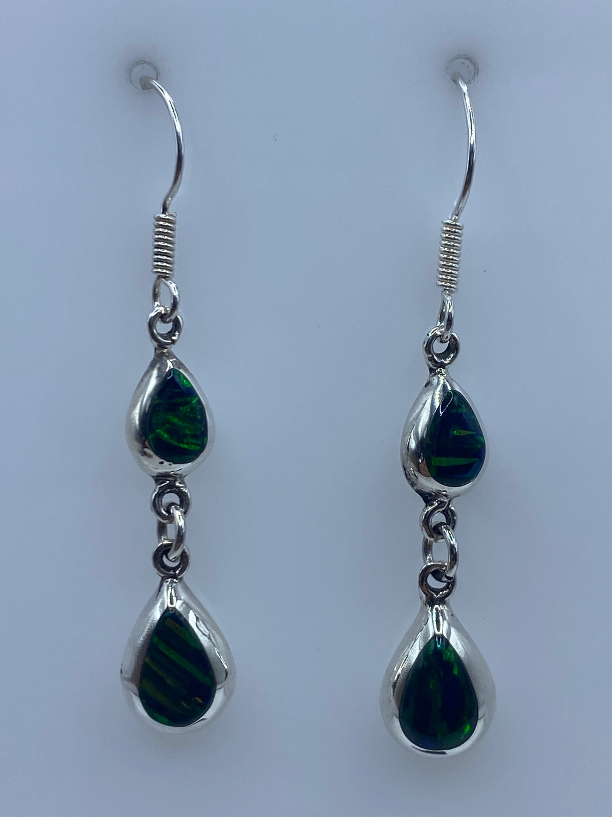 Par de aretes de plata con ópalo de fuego verde, colgando de un gancho