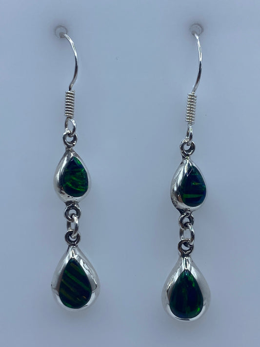 Par de aretes de plata con ópalo de fuego verde, colgando de un gancho