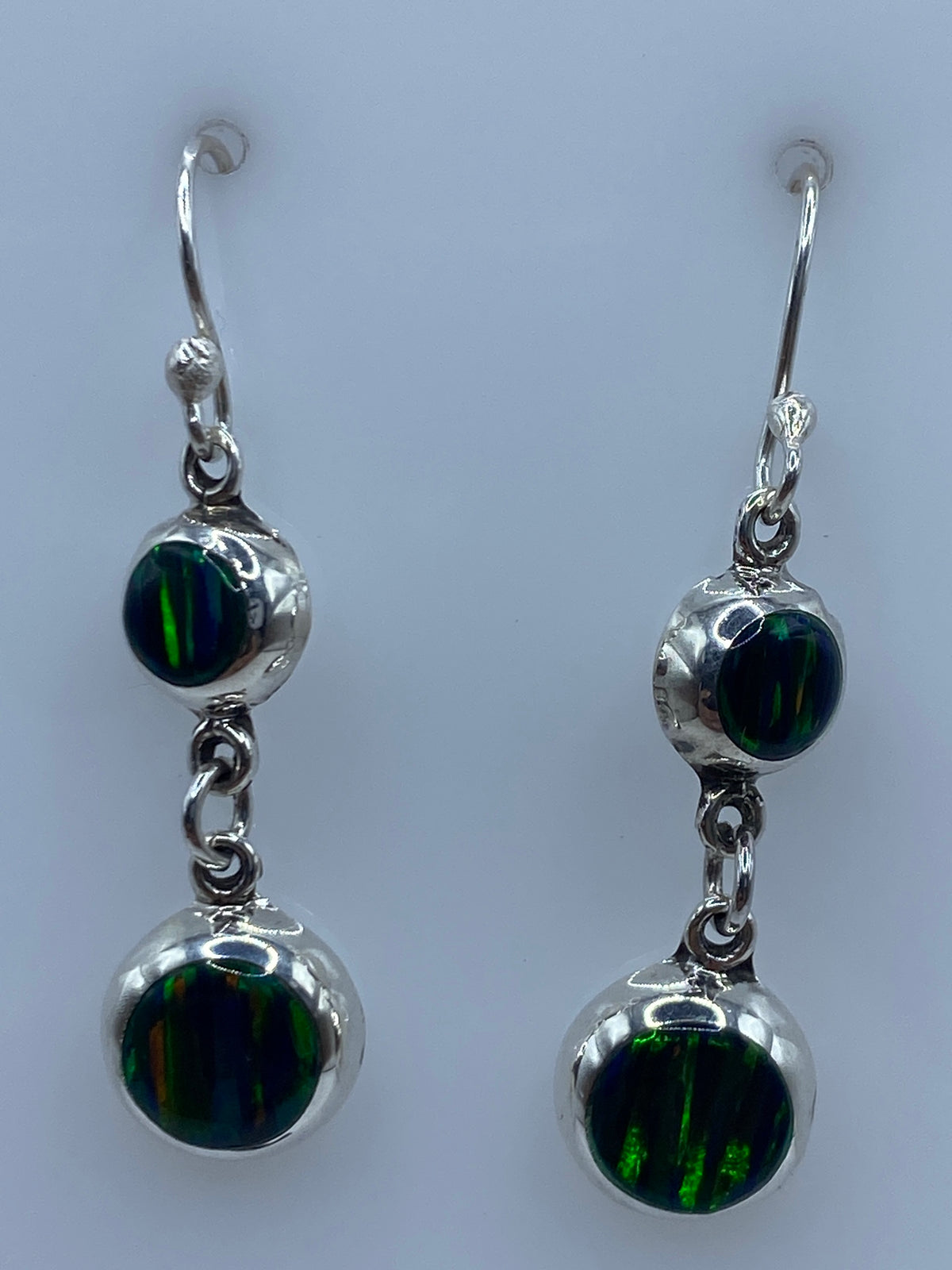 Aretes de plata con opalo de fuego engastado, largos 3.8 cm, colgados ante fondo azul