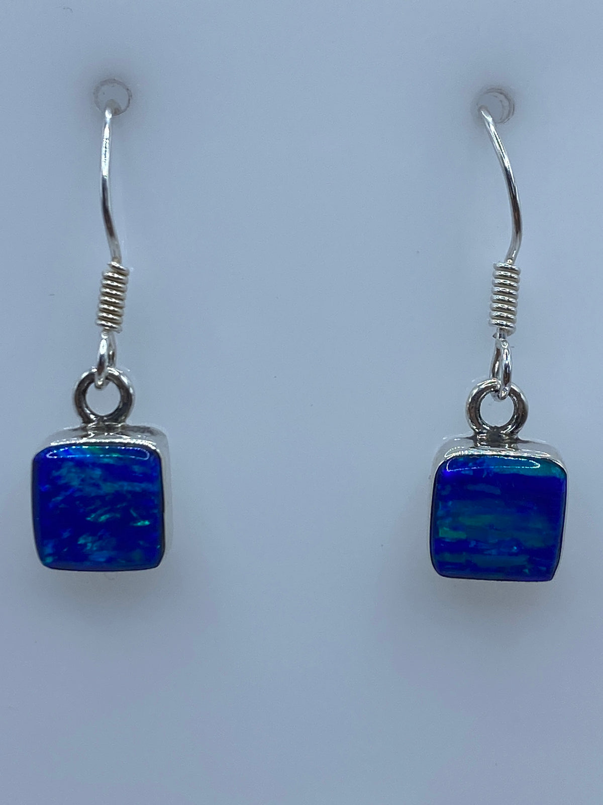 Par de aretes de plata 950 con Ópalo de Fuego azul engastado, 2.5 cm de largo, sobre fondo blanco