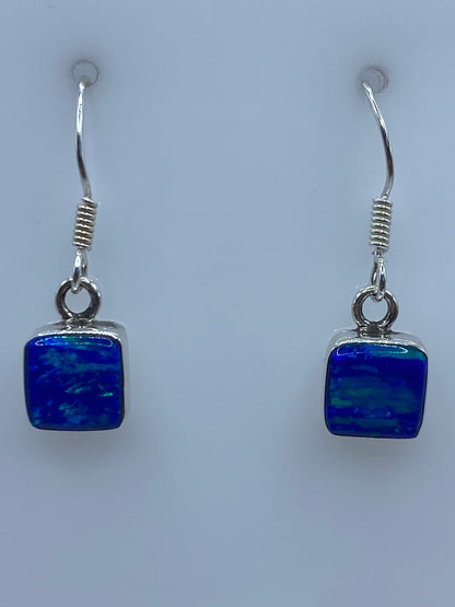 Par de aretes de plata 950 con Ópalo de Fuego azul engastado, 2.5 cm de largo, sobre fondo blanco