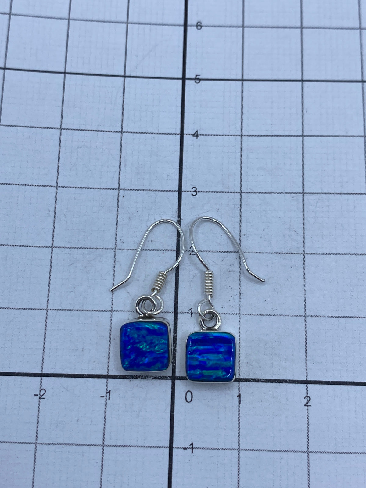 Aretes sobre regla de medición confirmando 2.5 cm de largo, con Quinto 950 visible