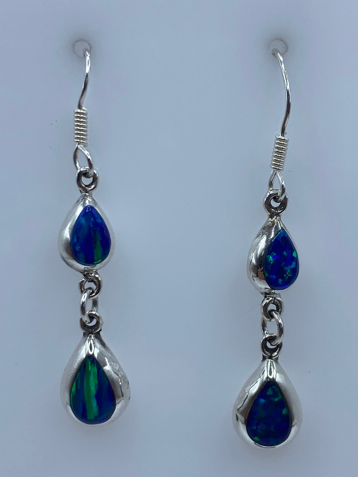 Par de aretes de plata 925 con ópalo de fuego azul engastados a mano, colgando sobre fondo neutro