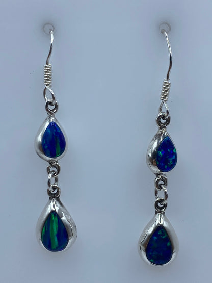 Par de aretes de plata 925 con ópalo de fuego azul engastados a mano, colgando sobre fondo neutro
