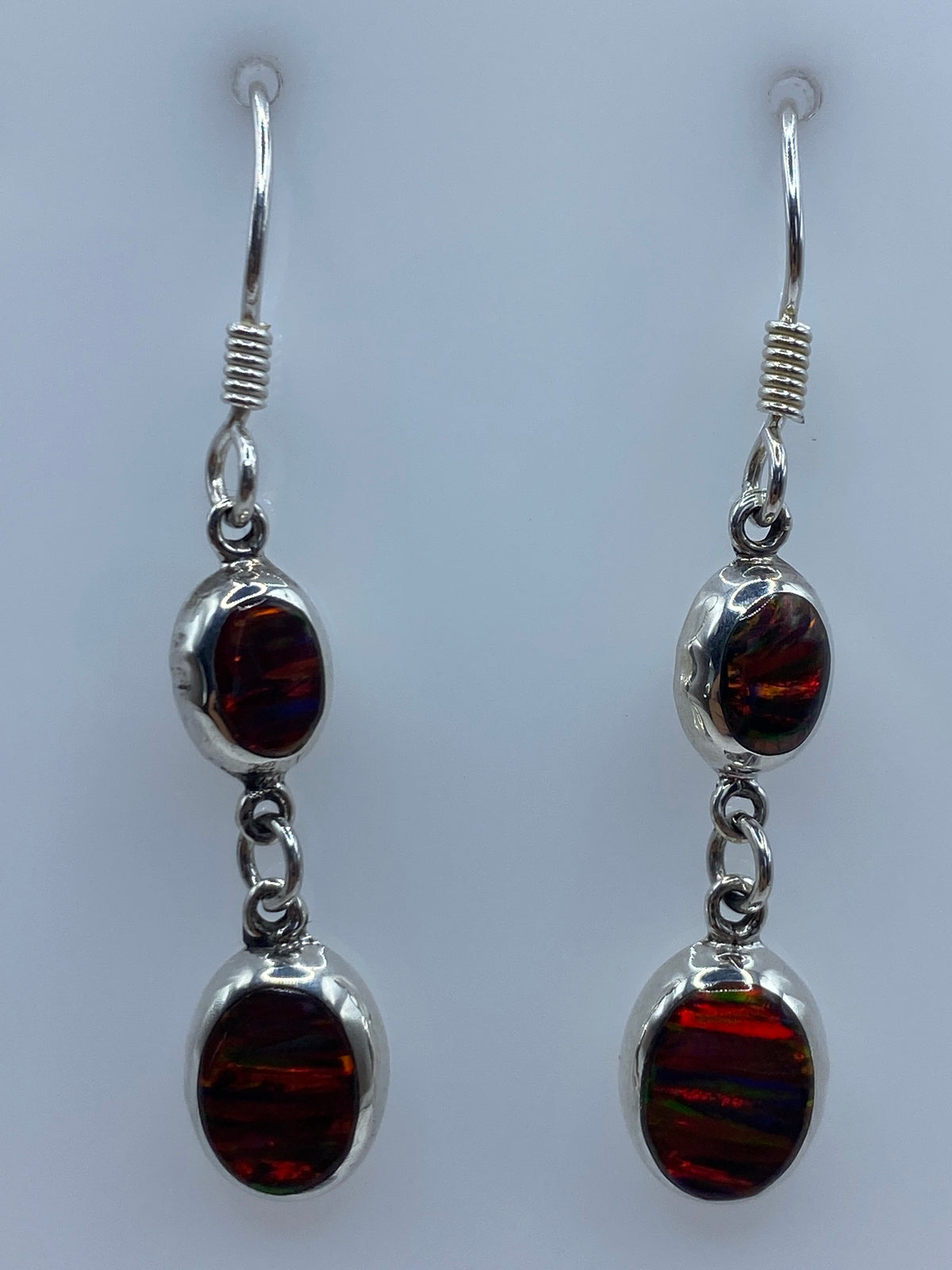 Par de aretes de plata con ópalo de fuego multicolor engastado, colgando sobre fondo gris