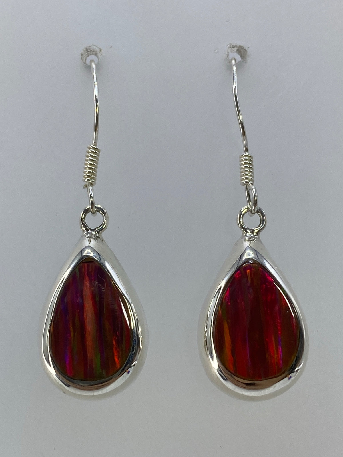 Par de aretes de plata con ópalo de fuego multicolor, largos 3.8 cm, colgando sobre fondo blanco