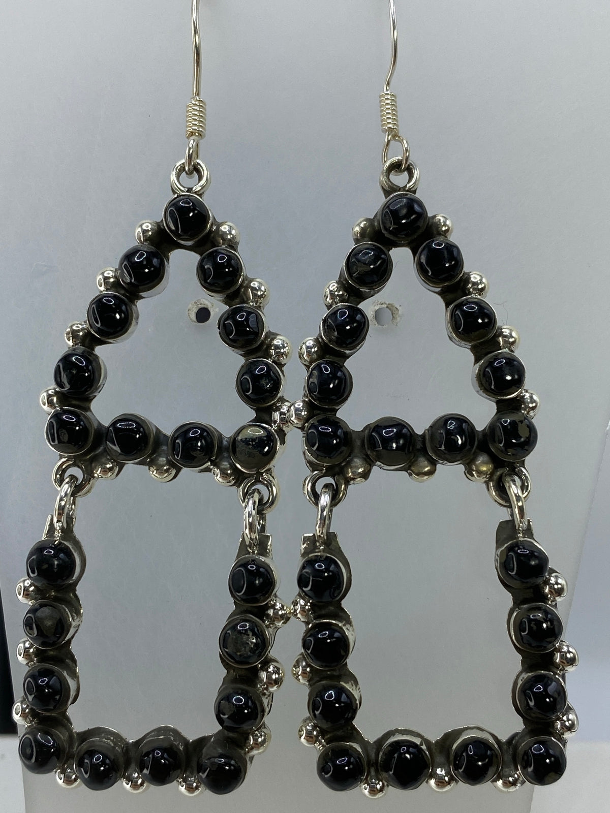Par de aretes largos de plata 925 con onix negro engastado en patrones geométricos, vistos en detalle frontal