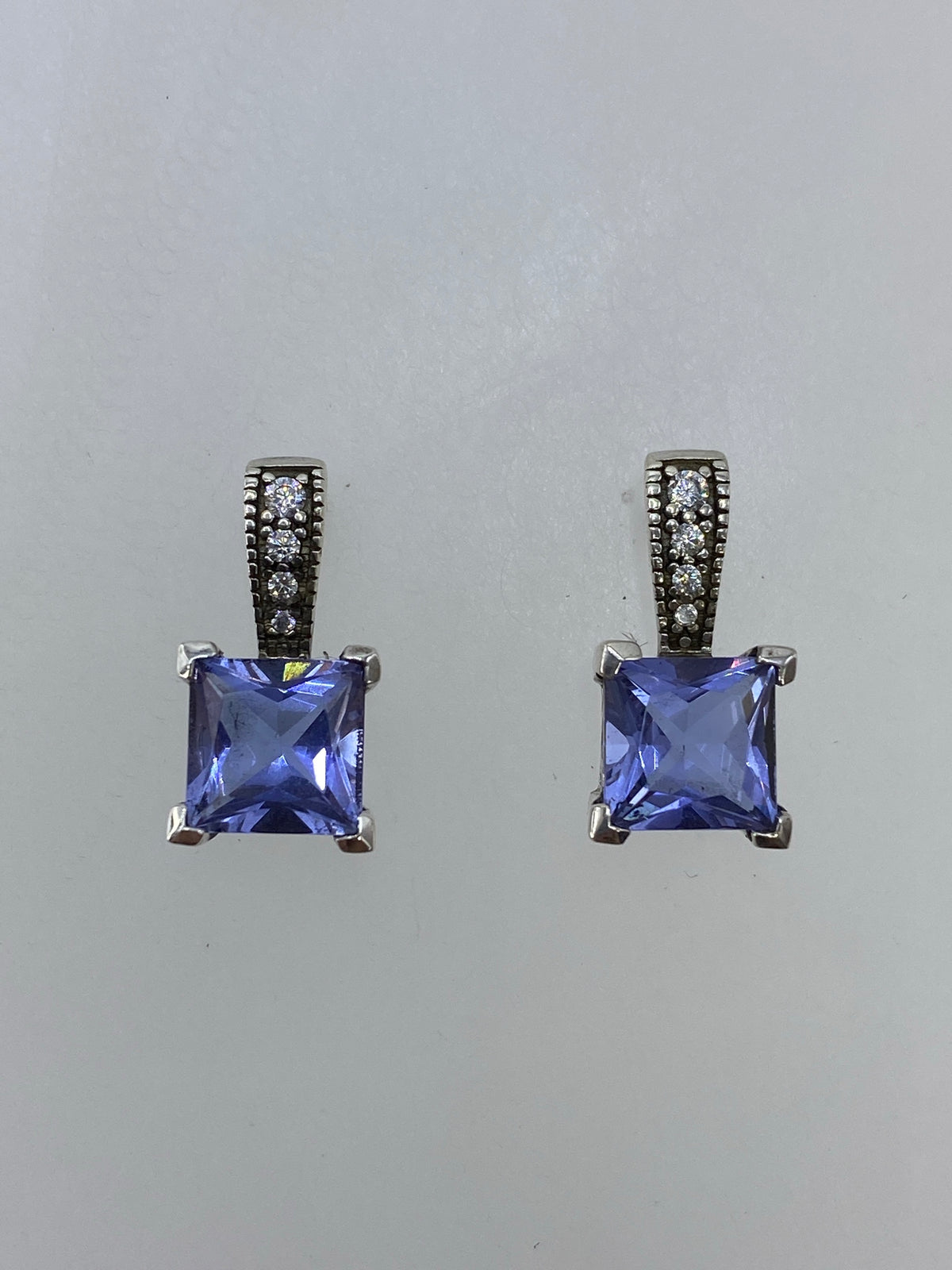 Par de aretes de plata 925 con circonia morada cuadrada, facetados, sobre fondo blanco