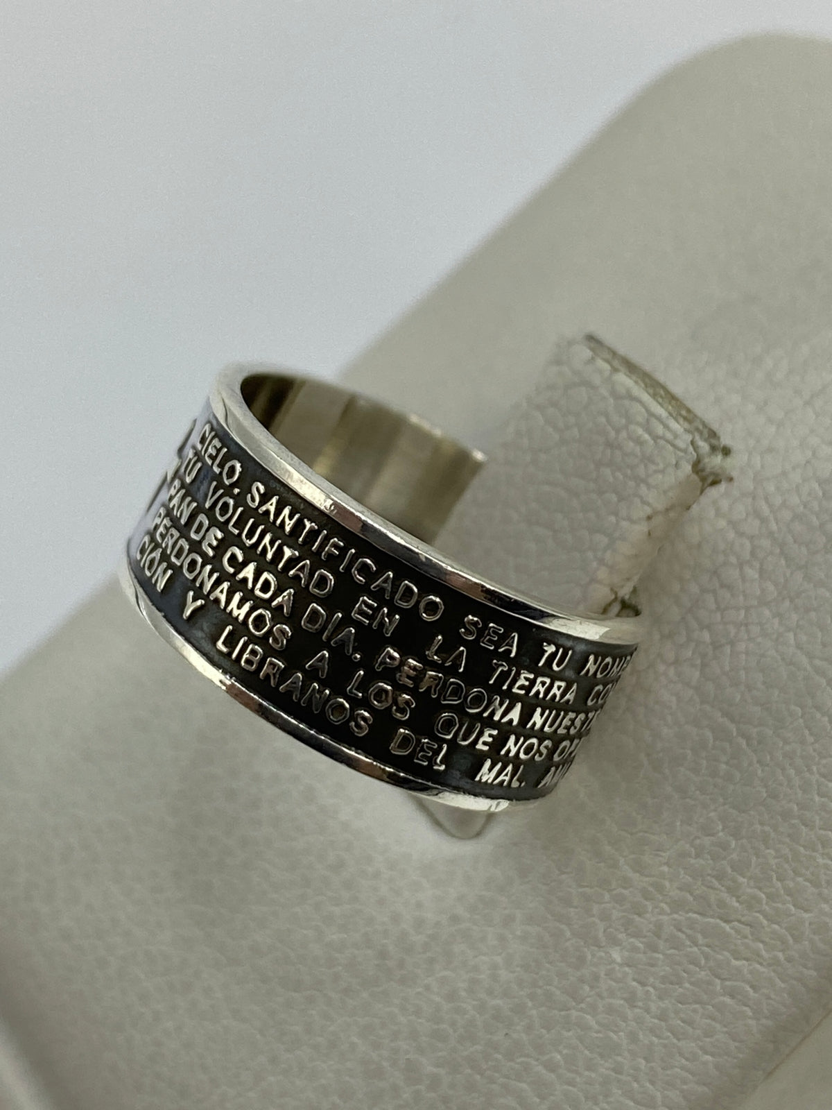 Anillo religioso de plata colocado en dedo, mostrando la legibilidad del texto