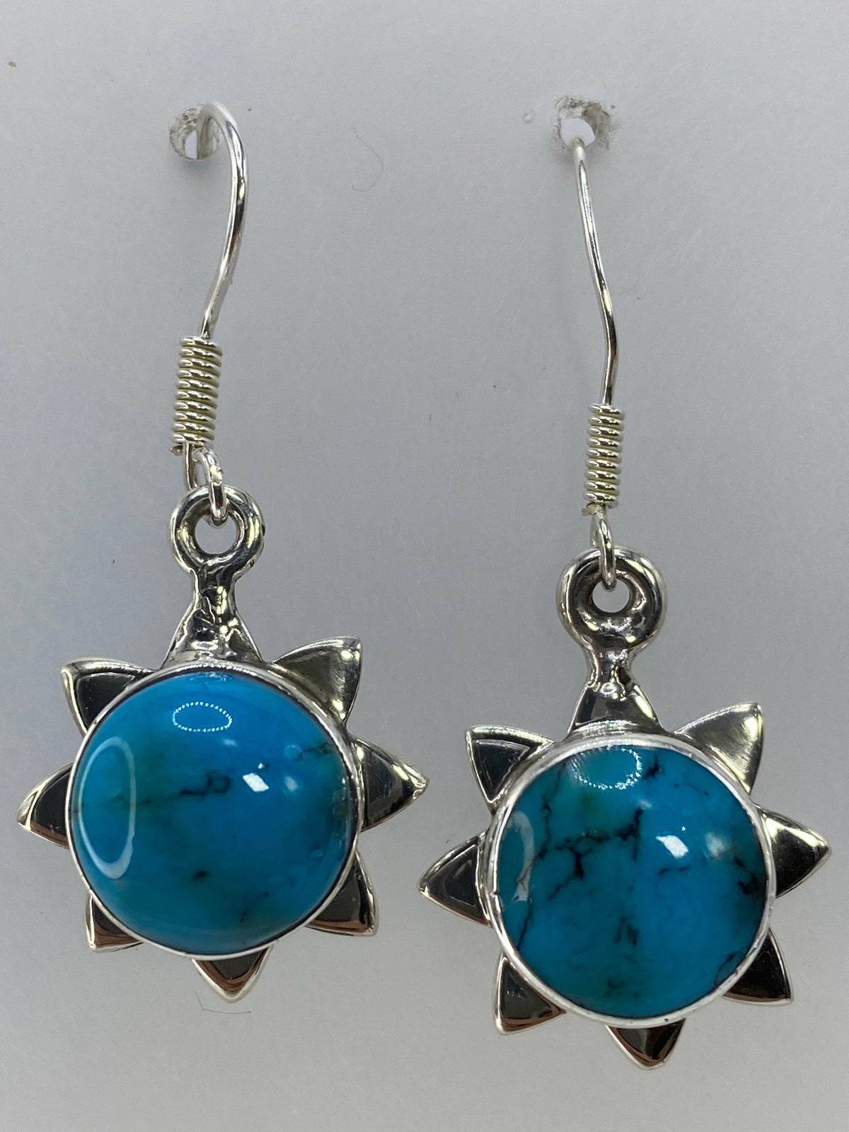 Aretes sol de plata posados sobre fondo blanco con el Quinto 925 visible