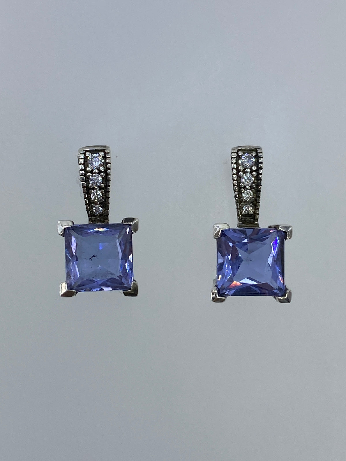 Par de aretes de plata con circonia azul engastada, vistos de frente sobre fondo gris