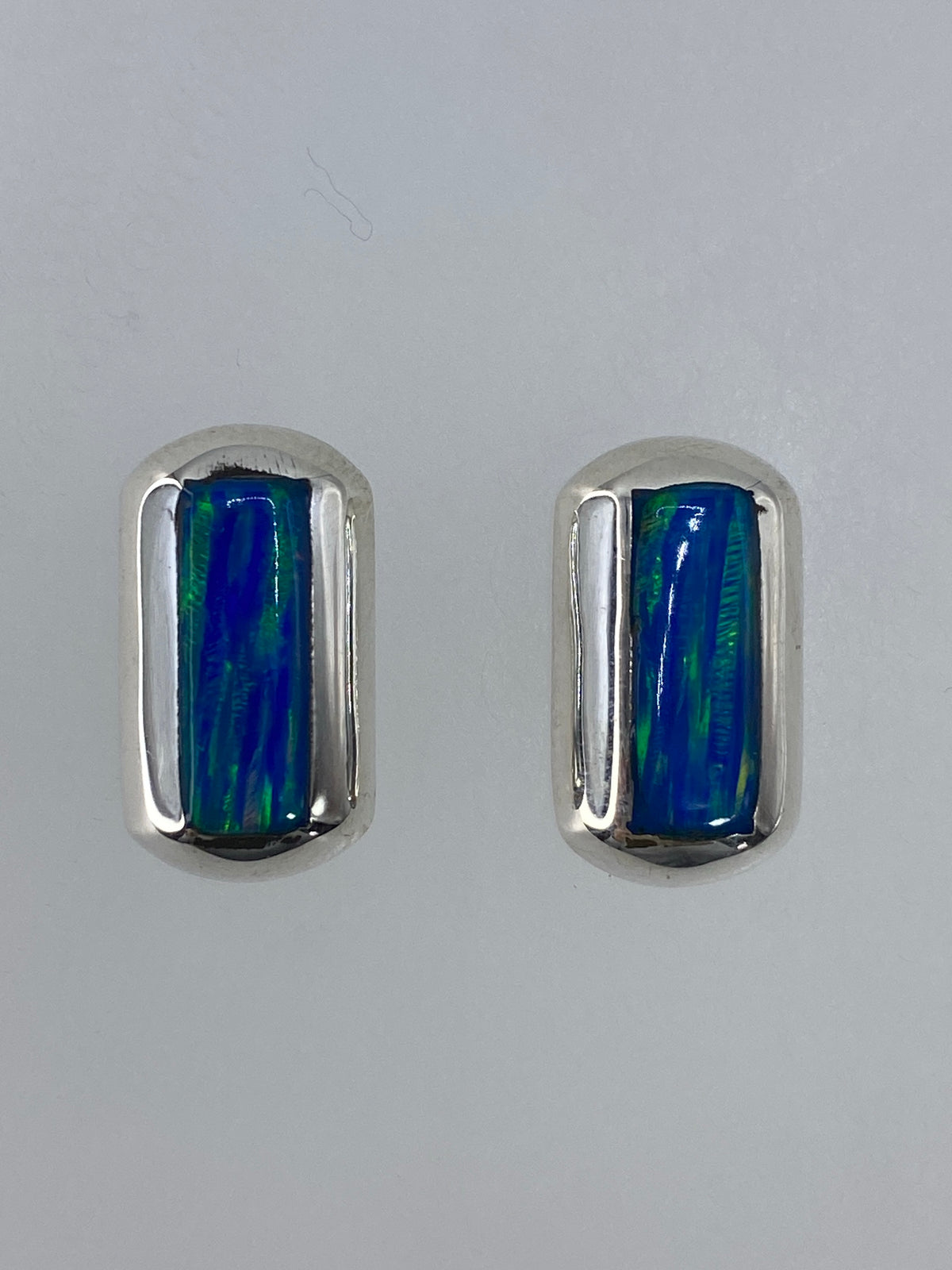 Aretes en ópalo de fuego sobre fondo blanco mostrando el reflejo multicolor