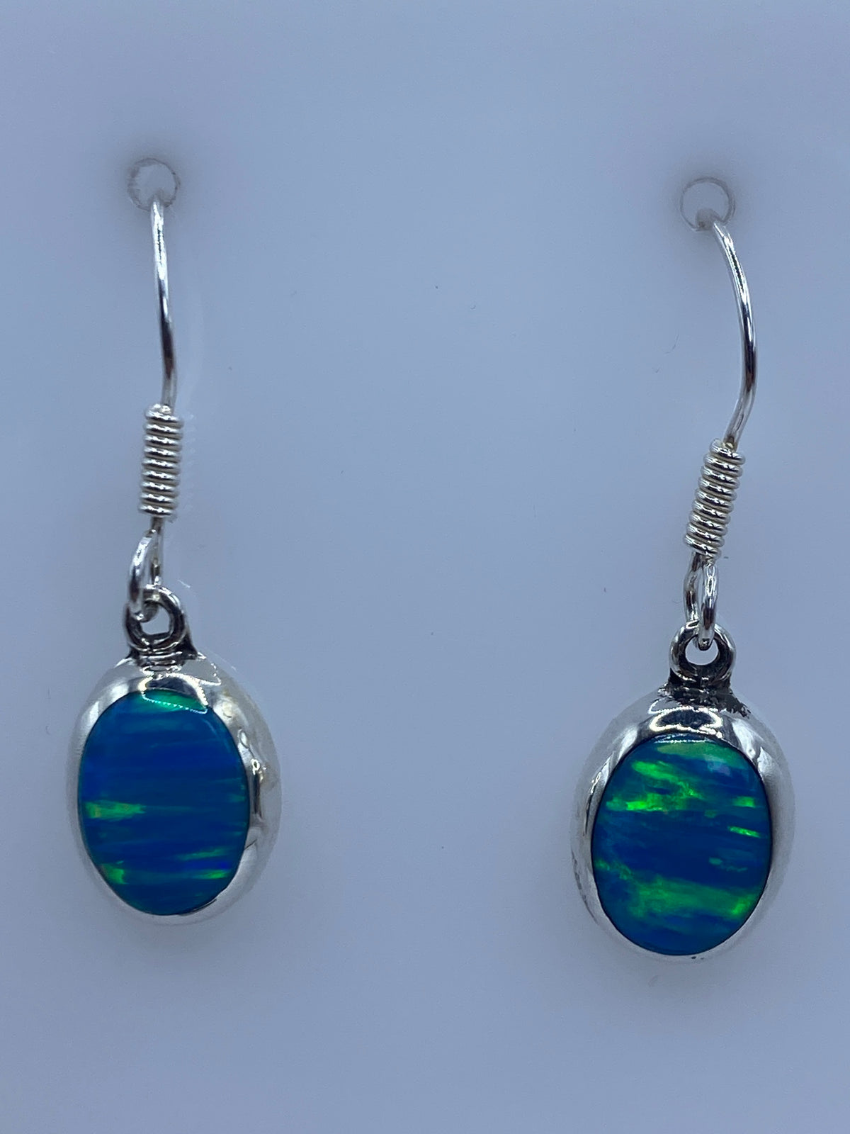 Par de aretes de plata con ópalo de fuego azul cielo, colgando sobre fondo blanco
