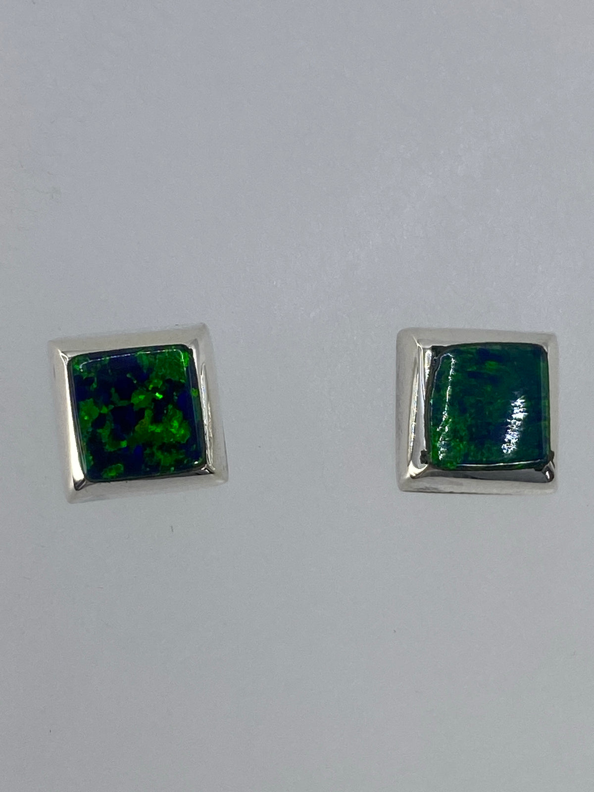 Par de aretes de plata con ópalo de fuego verde, vistos de frente sobre superficie blanca