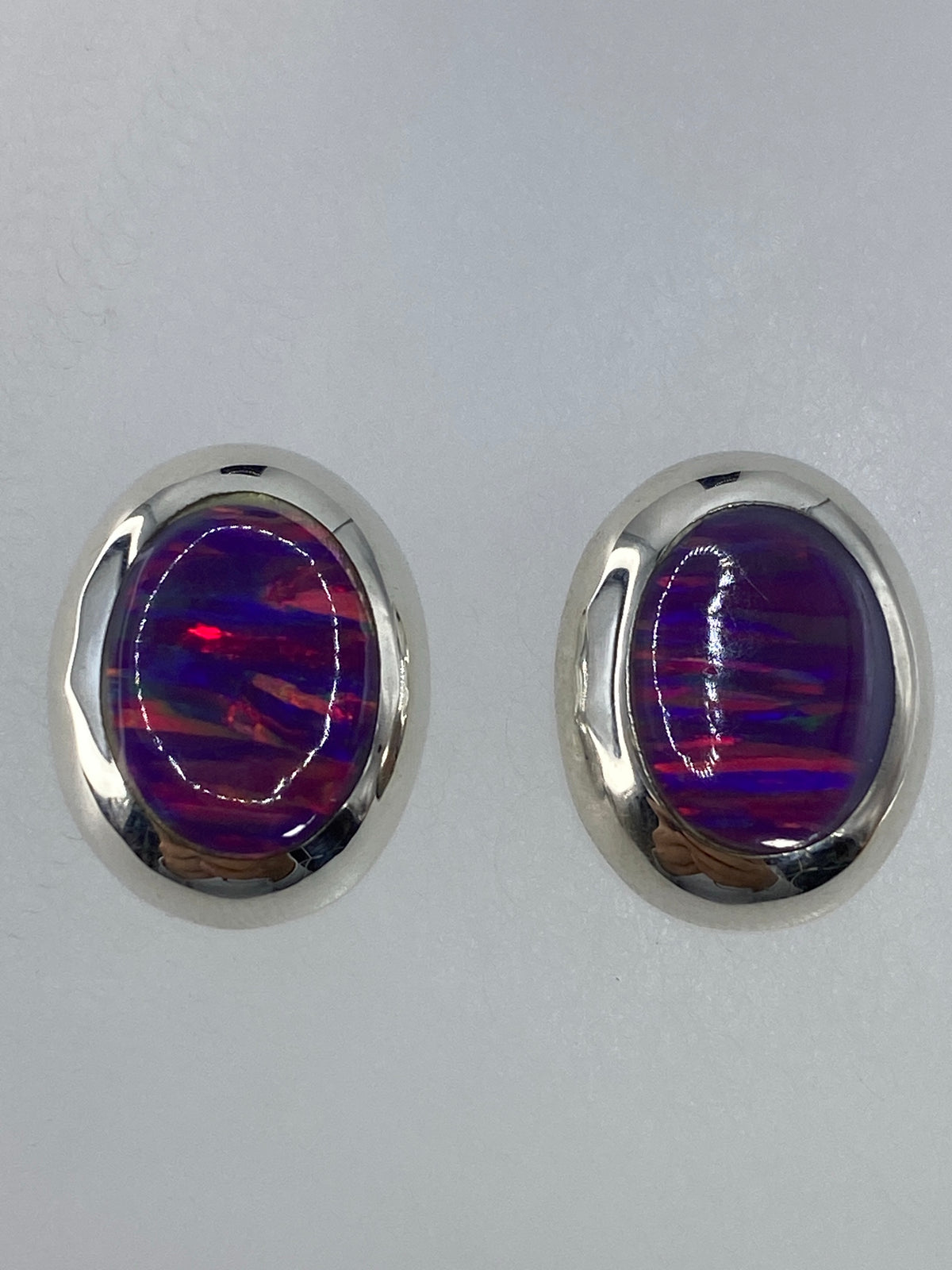 Aretes sobre fondo blanco mostrando los reflejos rojos, naranjas y amarillos del ópalo