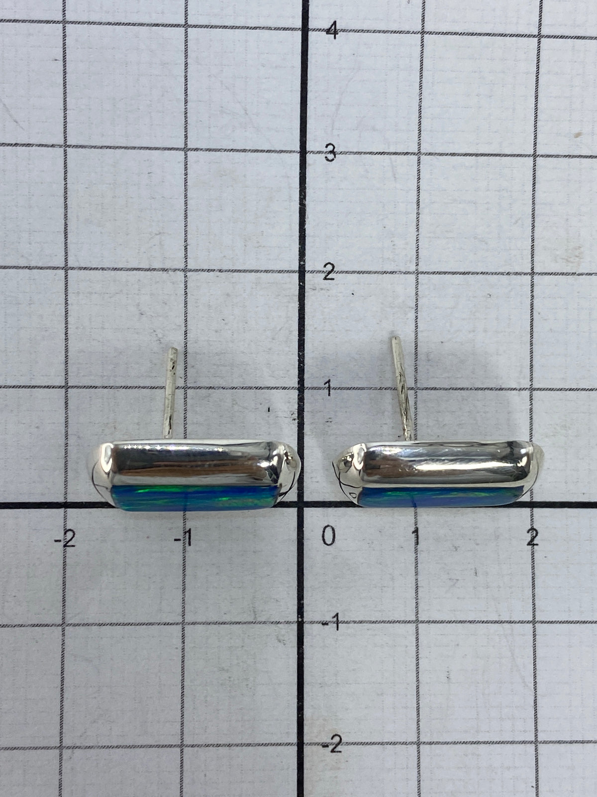 Medida comparativa de los aretes de 1.4 cm sobre regla de centímetros, con el Quinto 925 en la parte trasera
