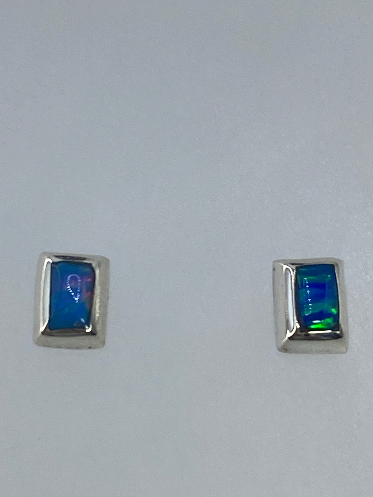 Aretes de plata del lado, evidenciando el delicado poste y el color multicolor de la piedra