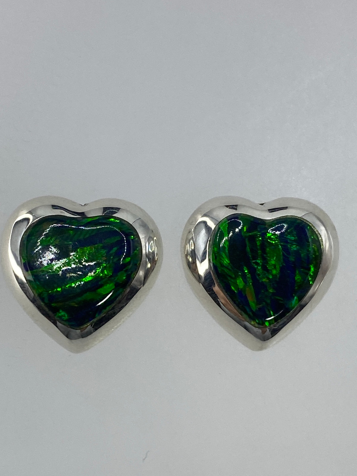 Aretes de plata con ópalo de fuego verde, vistos de frente sobre fondo blanco