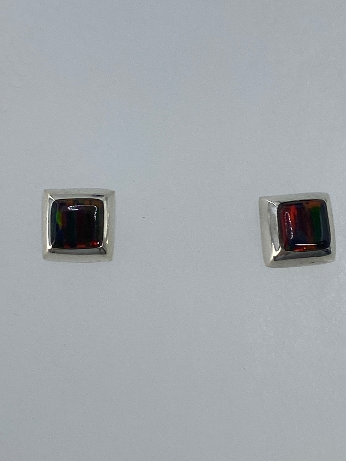 Par de aretes de plata con ópalo de fuego multicolor, largos 1.3 cm, sobre fondo blanco