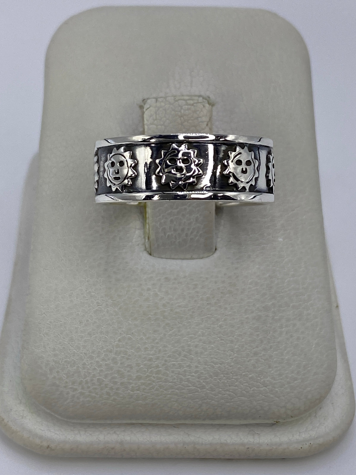 Anillo de plata repujado con calaveras prehispánicas en talla 7, mostrado en dedo pulgar
