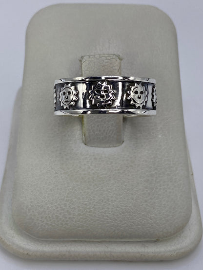 Anillo de plata repujado con calaveras prehispánicas en talla 7, mostrado en dedo pulgar