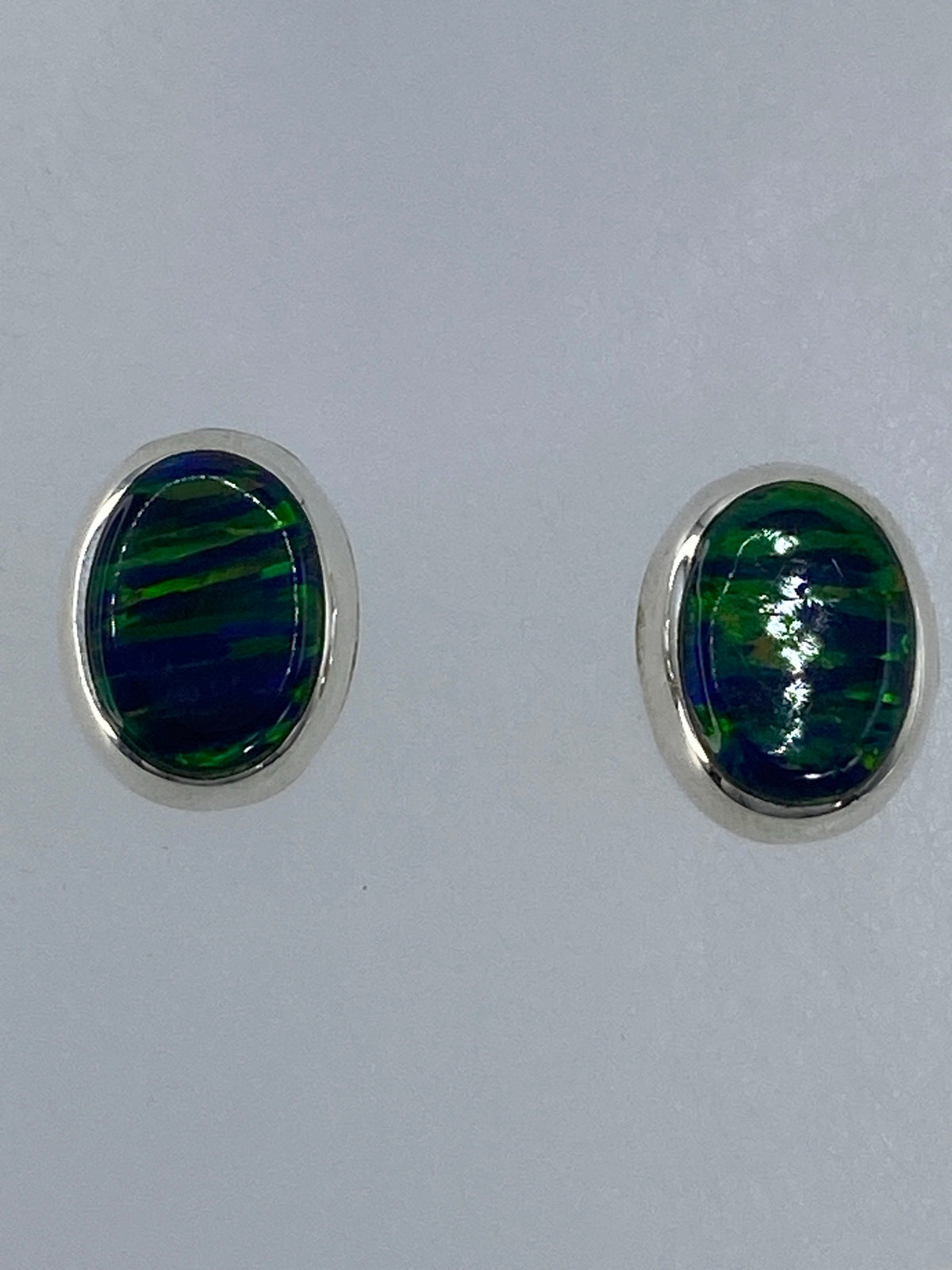 Vista frontal del par de aretes con el brillo característico del ópalo verde