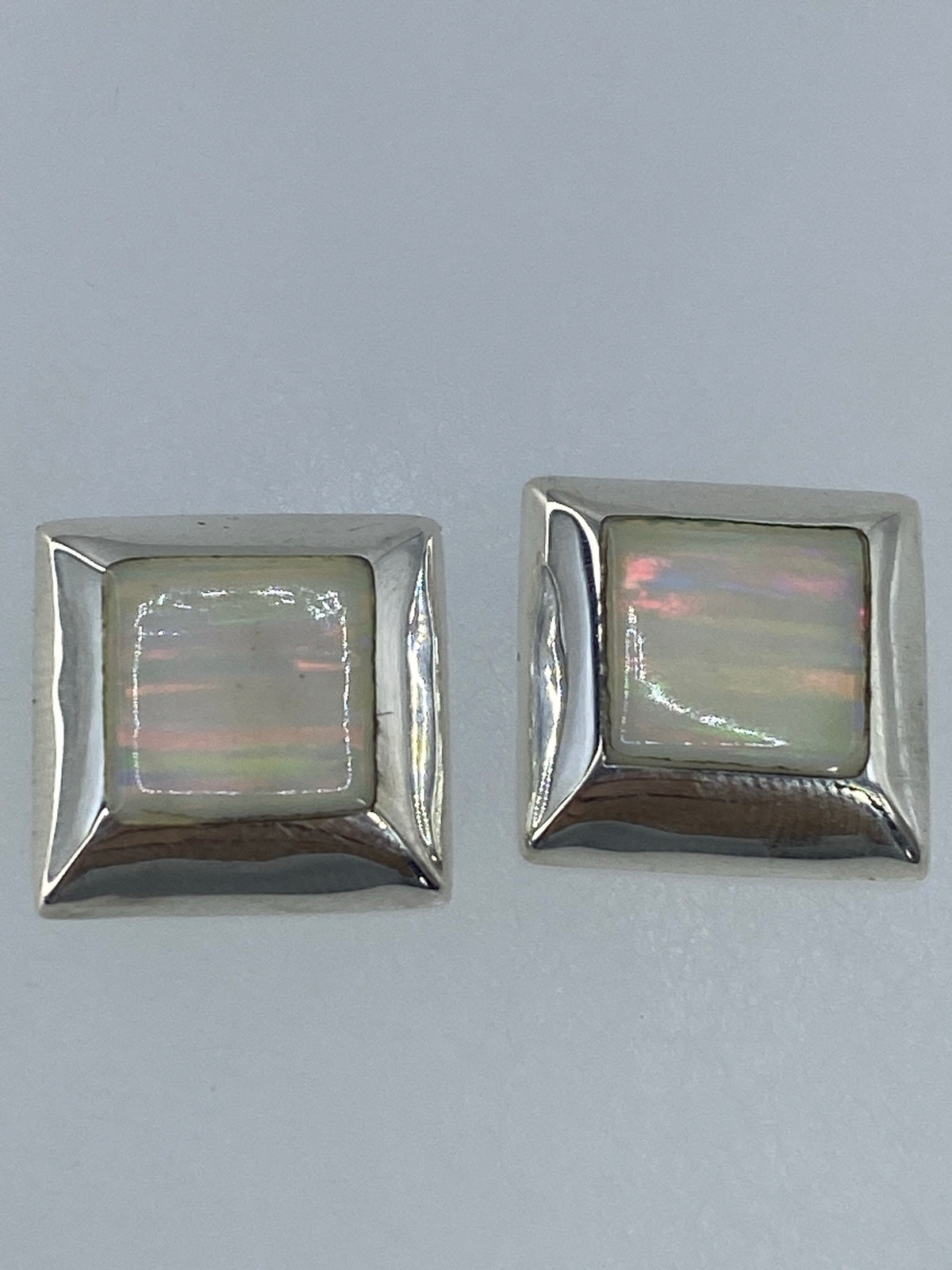 Aretes de opalo de fuego mostrando tonos rojos, naranjas y verdes bajo la luz