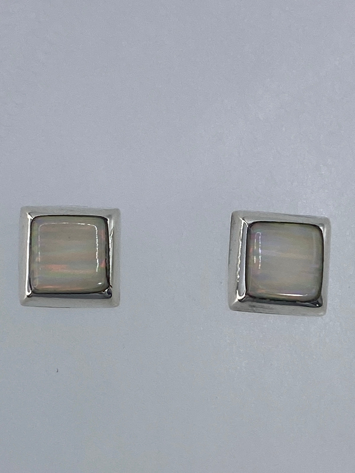 Par de aretes de plata con ópalo de fuego multicolor, vistos de frente sobre fondo gris
