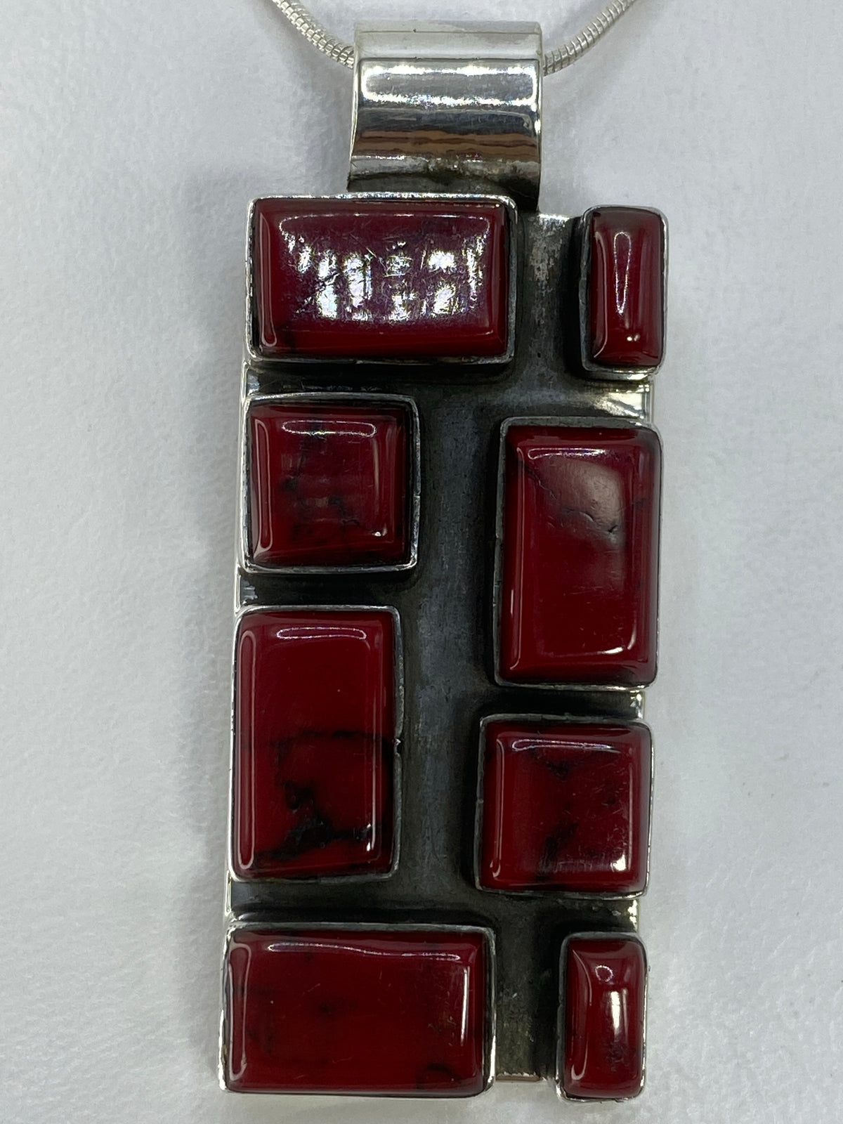 Dije de plata 950 con incrustación de piedra roja, vista frontal mostrando el apilado geométrico