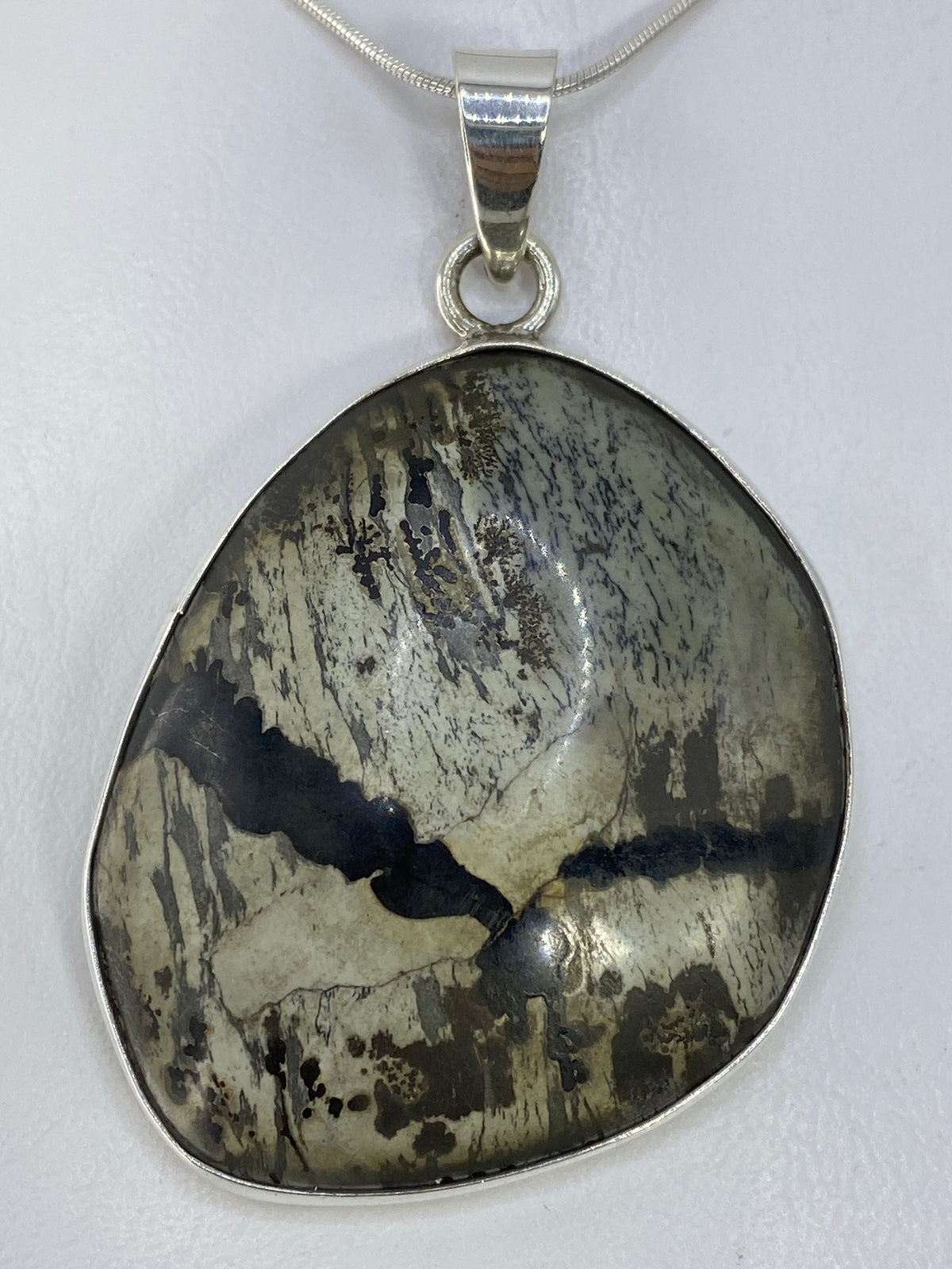 Dije de plata 925 con incrustación de piedra natural en tonos grises y negros, colgado de cadena plateada