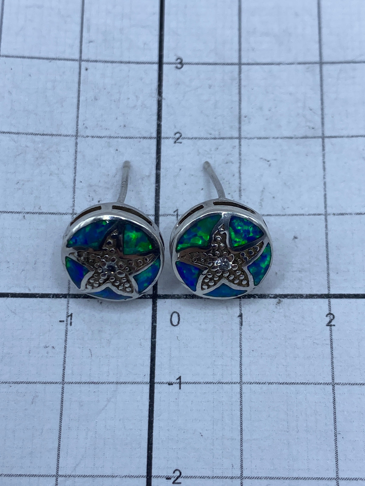Par de aretes de plata ópalo azul junto a regla de medida en centímetros