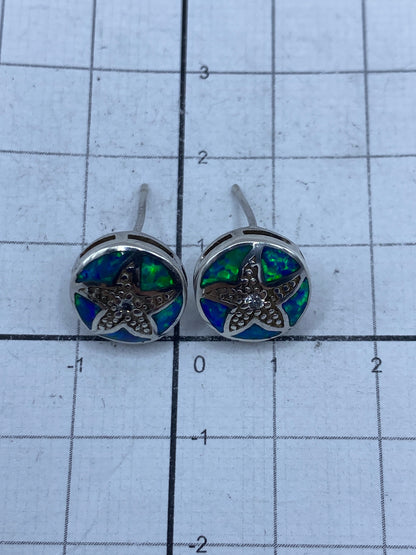 Par de aretes de plata ópalo azul junto a regla de medida en centímetros