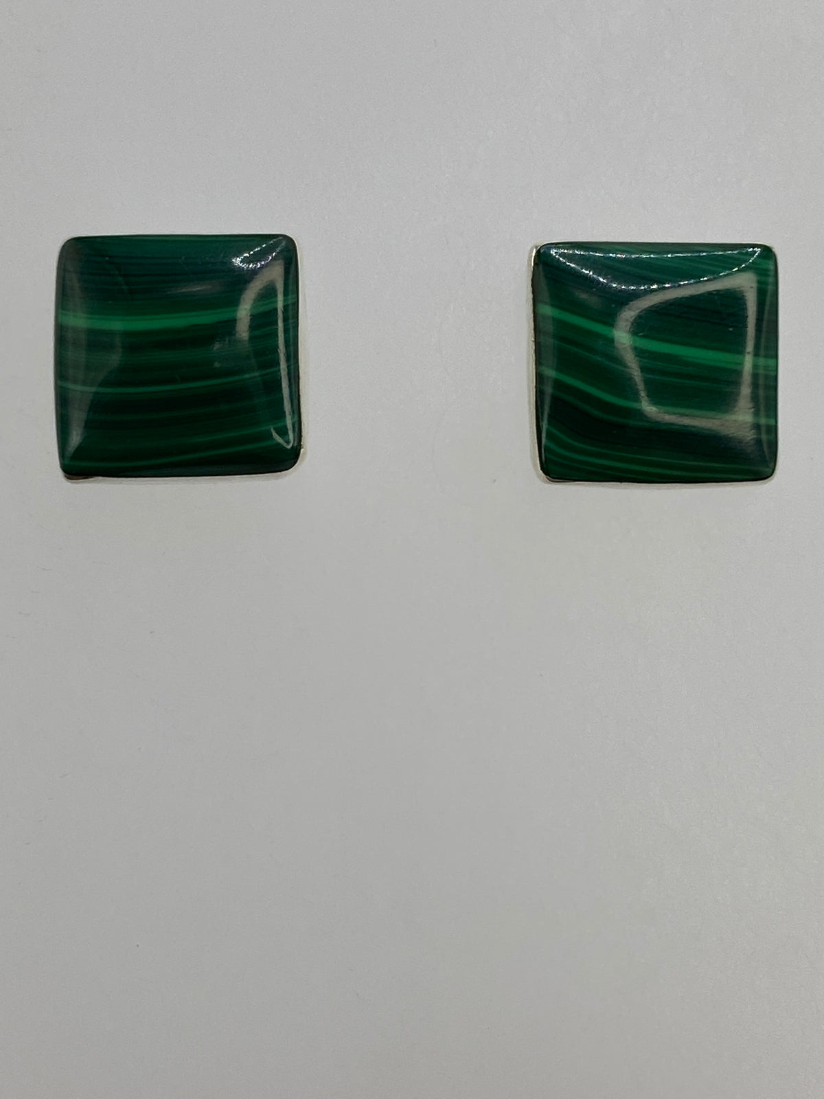 Aretes con malaquita en la mano, mostrando el tamaño discreto y el brillo de la plata 950