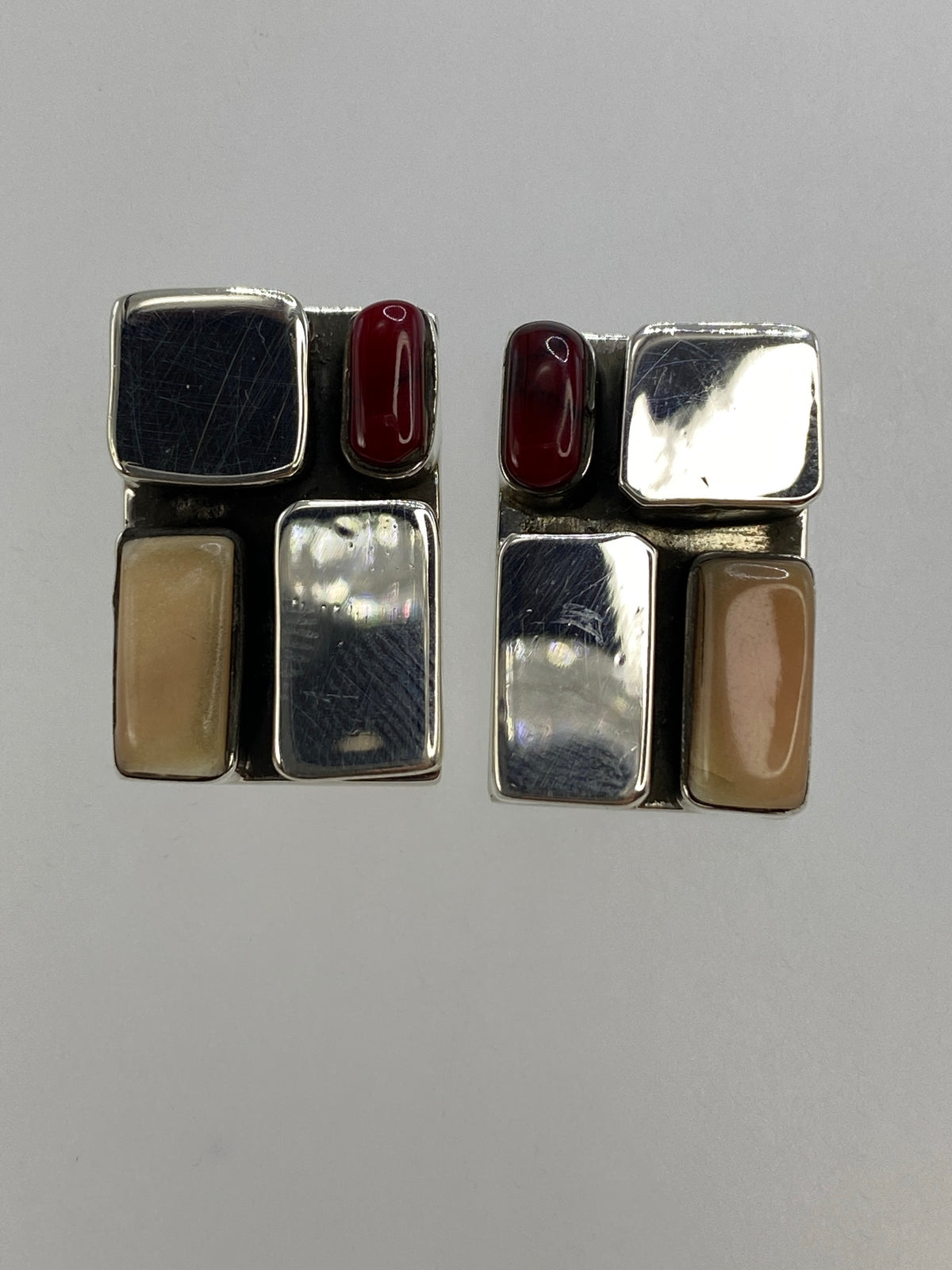 Par de aretes de plata con coral blanco y rojo, vista frontal sobre fondo gris