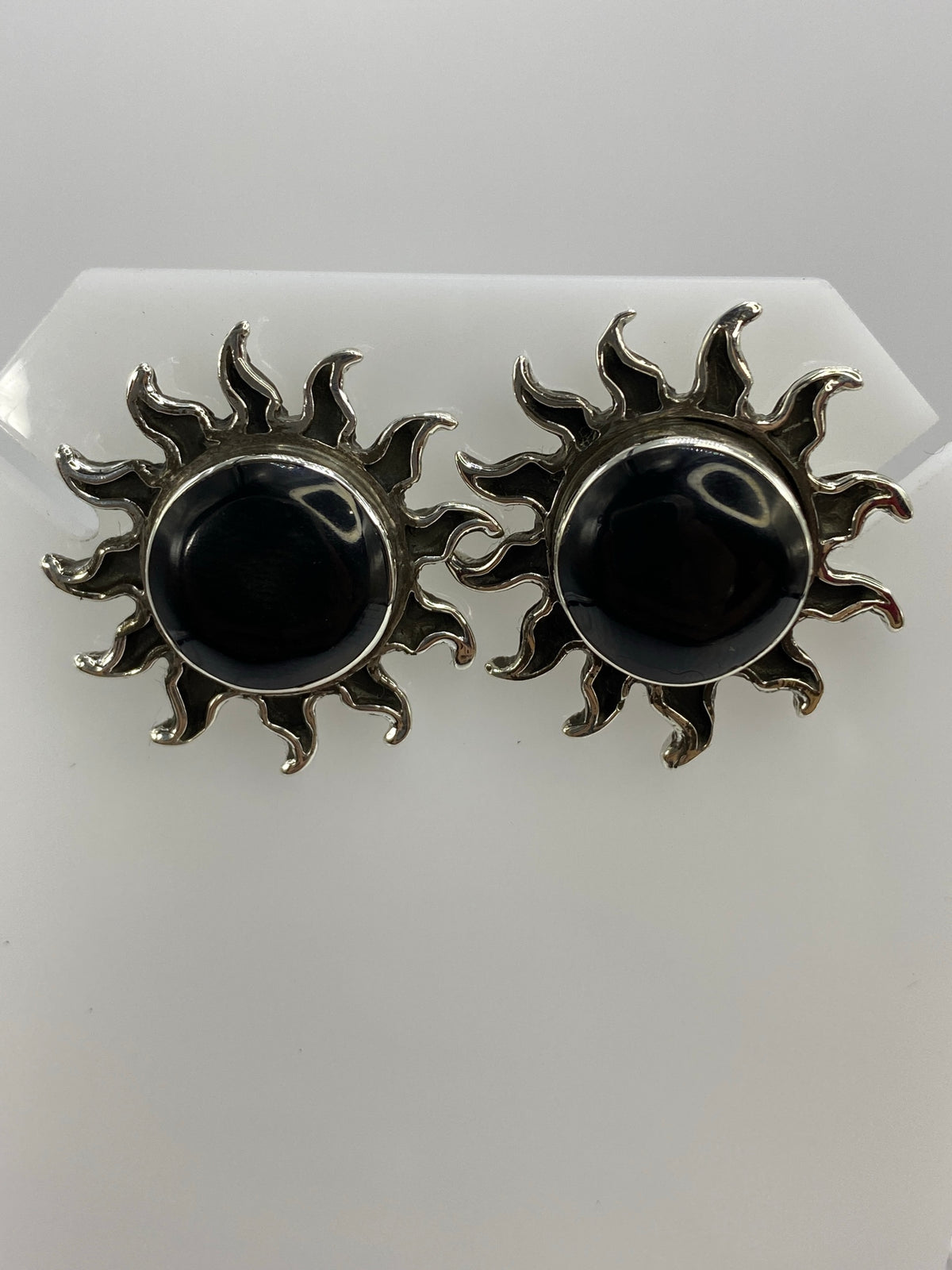 Aretes de plata en forma de sol con ónix negro engastado en el centro, vista frontal