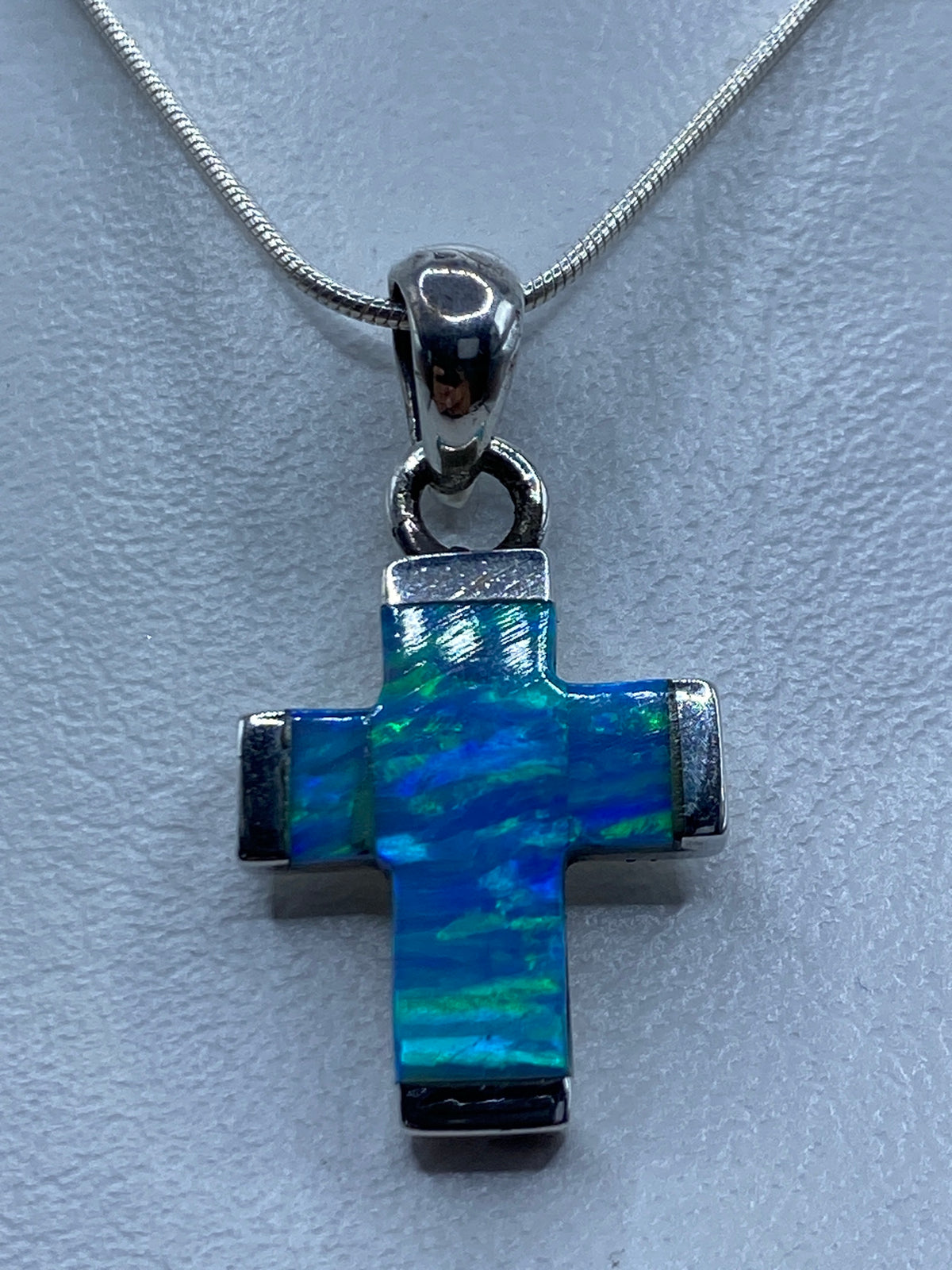 Detalle frontal del ópalo azul incrustado en la cruz de plata, mostrando reflejos de luz