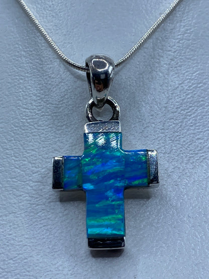 Detalle frontal del ópalo azul incrustado en la cruz de plata, mostrando reflejos de luz