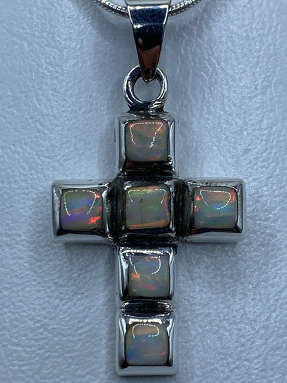 Vista frontal del dije cruz: plata pulida con piedra de color tornasol en el centro